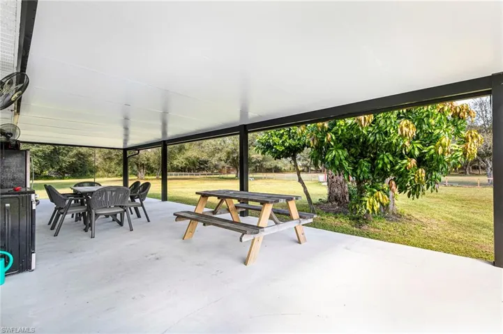 Covered patio featuring a concrete floor, dark structural supports, and a expansive backyard with mature trees