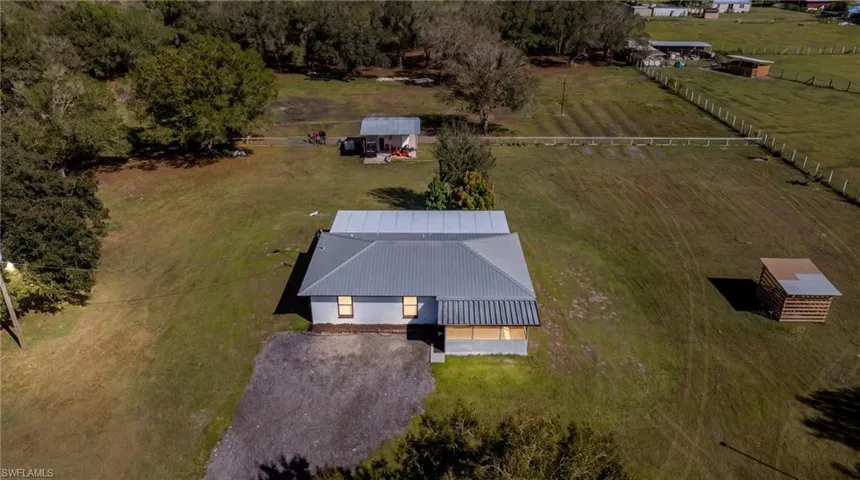 Expansive acreage featuring a metal-roofed residence, a detached secondary structure, a gravel driveway, and a fenced perimeter