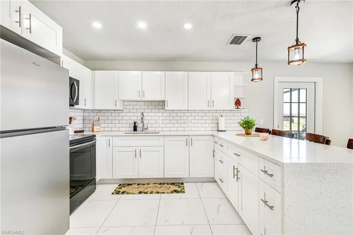 Kitchen featuring white shaker-style cabinetry, quartz countertops, a subway tile backsplash, stainless steel appliances, and large-format tile flooring