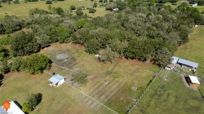 Aerial perspective of expansive acreage featuring mature tree clusters, cleared pasture land, perimeter fencing, and multiple detached outbuildings