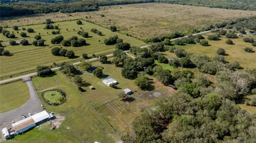 Expansive acreage featuring cleared pasture land, clusters of mature trees, a private pond, and gravel driveways