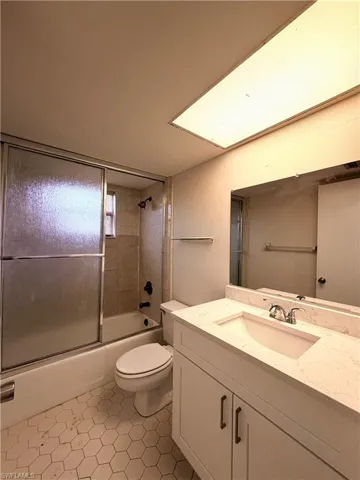 Bathroom featuring a white vanity with a light-colored countertop and integrated sink, a rectangular mirror, and a bathtub with sliding glass doors and tiled surround