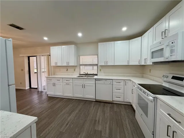 Bright kitchen featuring white cabinetry, light countertops, wood-finish flooring, recessed lighting, and a full suite of white appliances