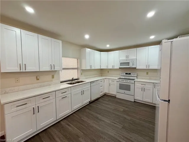Spacious kitchen featuring white shaker-style cabinetry, light-toned countertops, wood-finish flooring, a double basin sink, and recessed lighting