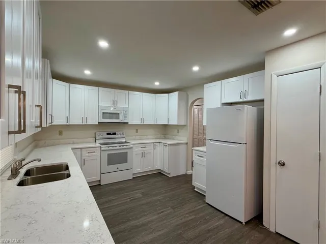 Renovated kitchen featuring white cabinetry, light-toned countertops, a dual-basin stainless steel sink, and wood-finish flooring