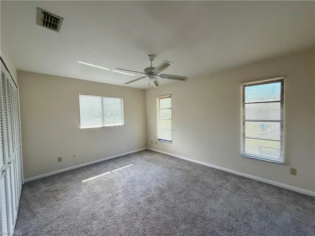 Carpeted room featuring multiple windows with blinds, a ceiling fan with light fixture, and a built-in closet with louvered bifold doors