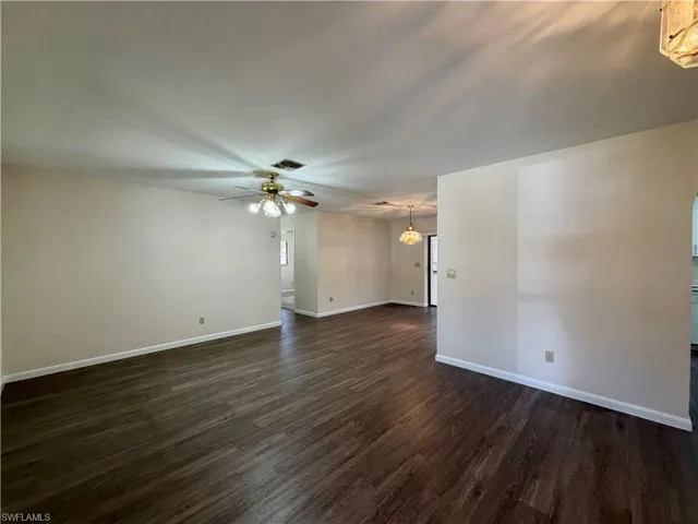 Spacious interior featuring wood-finish flooring, light neutral wall tones, a ceiling fan with integrated lighting, recessed lighting, and a prominent wall