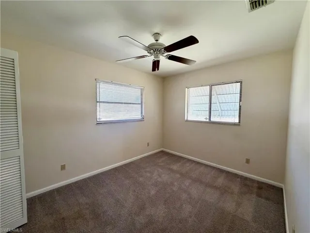 Carpeted interior room featuring a ceiling fan with wood-finish blades, two windows with blinds, a louvered bi-fold door, and light-toned walls