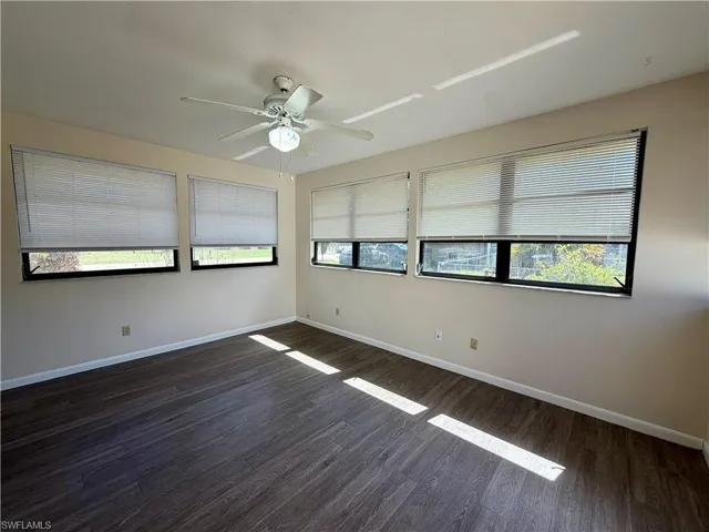 Room featuring wood-finish flooring, a ceiling fan with integrated lighting, and multiple windows with blinds