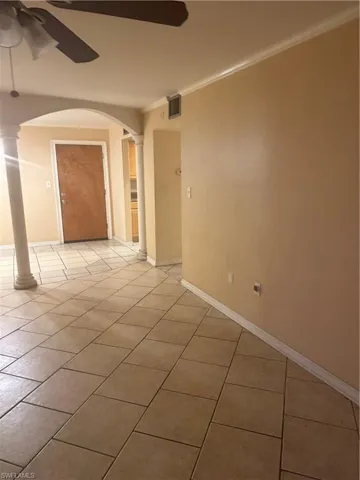 Spare room with a ceiling fan, crown molding, light tile patterned floors, arched walkways, and ornate columns