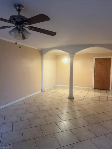 Spare room featuring ceiling fan, ornamental molding, ornate columns, arched walkways, and light tile patterned flooring