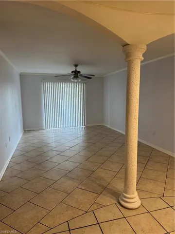 Spare room with ornate columns, crown molding, a ceiling fan, arched walkways, and light tile patterned flooring