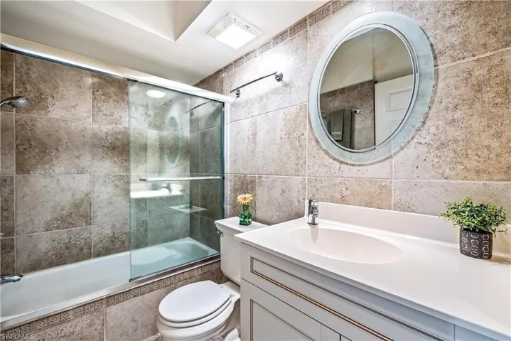 Full bathroom with vanity, toilet, tile walls, and bath / shower combo with glass door