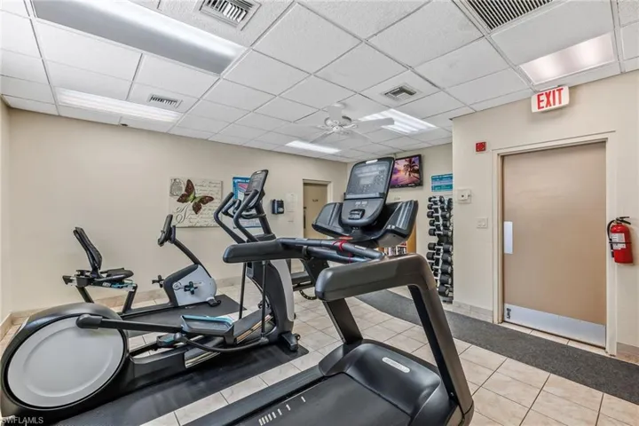 Exercise room featuring ceiling fan, a drop ceiling, and light tile patterned floors