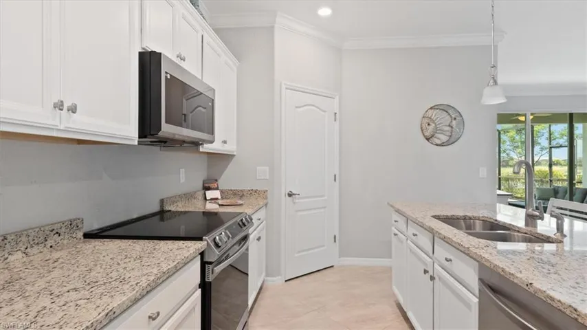 Kitchen featuring stainless steel appliances, white cabinetry, crown molding, hanging light fixtures, and light stone counters