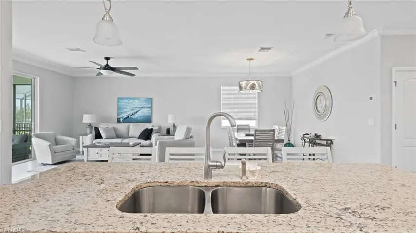 Kitchen featuring crown molding, light stone countertops, ceiling fan, decorative light fixtures, and open floor plan