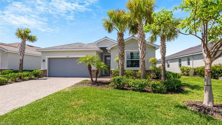 Florida ranch-style home with a front lawn, stucco siding, decorative driveway, an attached garage, and stone siding