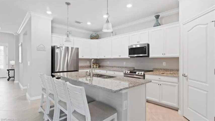 Kitchen with light stone countertops, a breakfast bar area, a center island with sink, stainless steel appliances, and white cabinets
