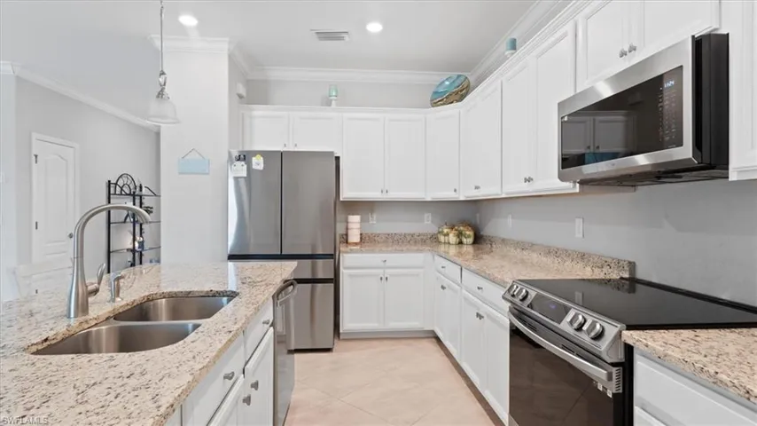 Kitchen featuring stainless steel appliances, white cabinetry, hanging light fixtures, and crown molding