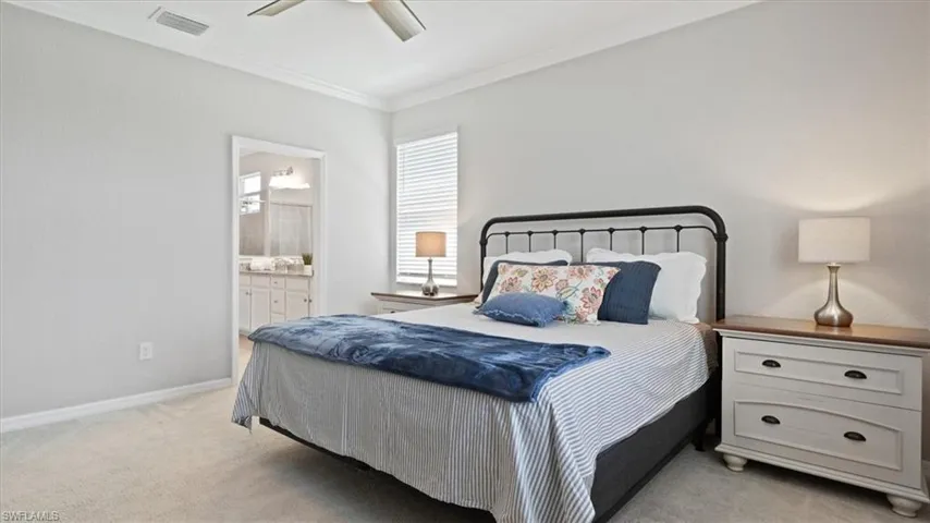 Bedroom featuring light colored carpet, ornamental molding, a ceiling fan, and ensuite bathroom