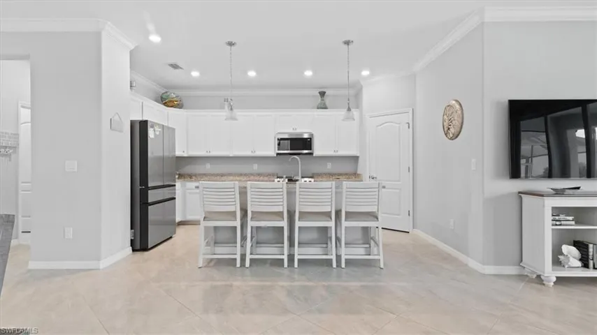 Kitchen with a breakfast bar area, hanging light fixtures, stainless steel appliances, a center island with sink, and white cabinets
