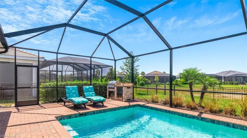 Outdoor pool featuring glass enclosure, a sunroom, exterior kitchen, and a patio area