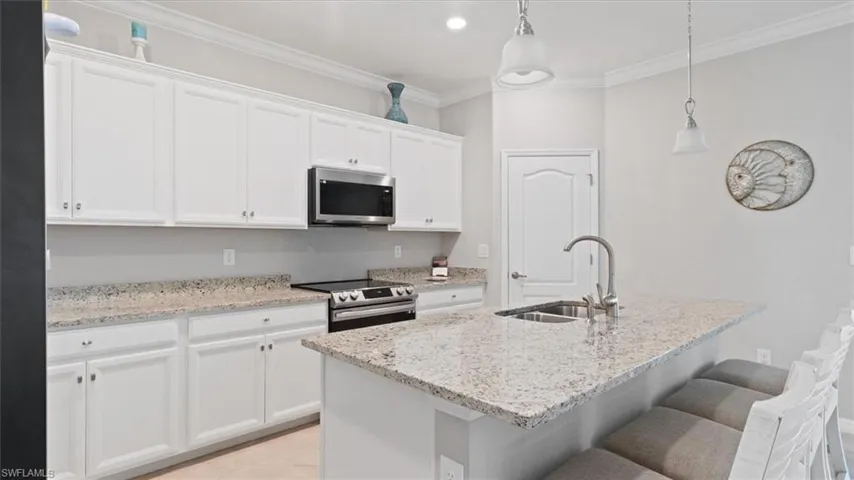 Kitchen featuring decorative light fixtures, stainless steel appliances, light stone counters, crown molding, and white cabinetry