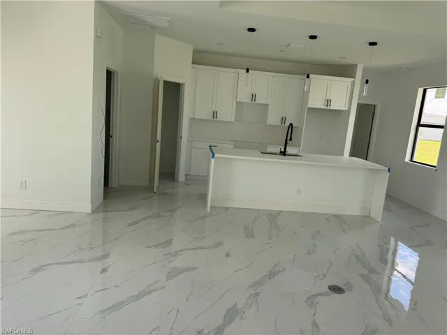 Kitchen featuring light marble finish floors, a kitchen island with sink, light stone counters, white cabinetry, and hanging light fixtures