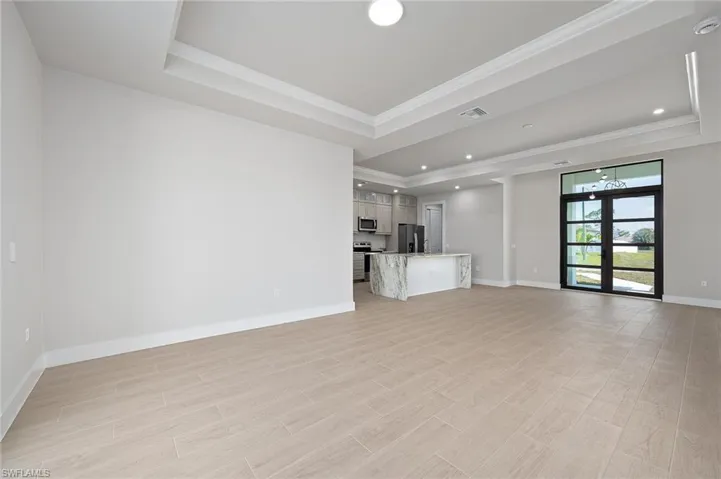 Unfurnished living room featuring a tray ceiling, french doors, and crown molding