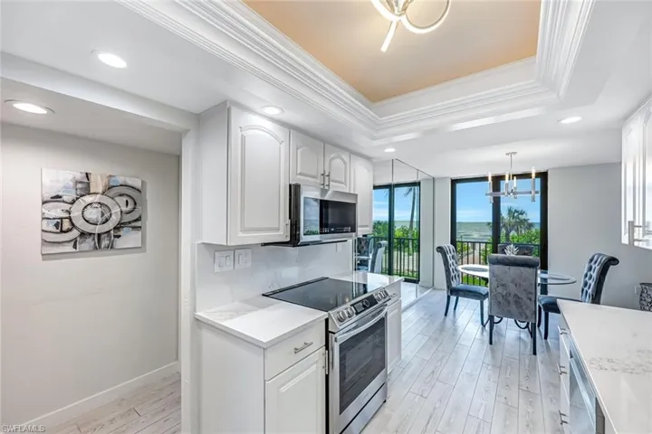 Kitchen with stainless steel appliances, a tray ceiling, light wood-style floors, crown molding, and a chandelier