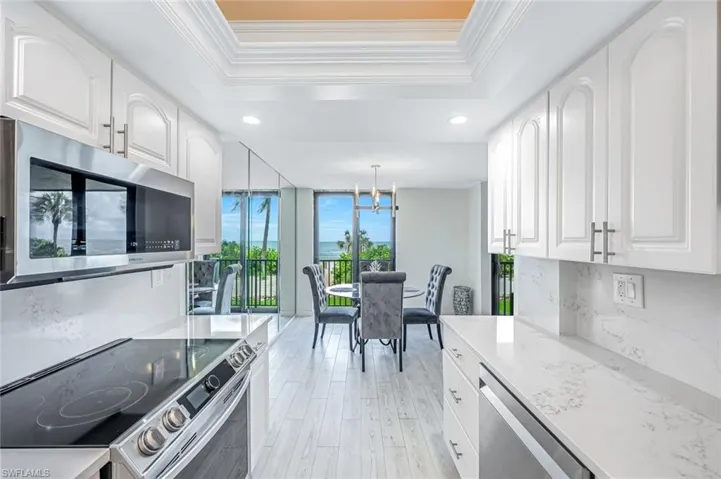 Kitchen featuring a raised ceiling, appliances with stainless steel finishes, white cabinets, ornamental molding, and recessed lighting