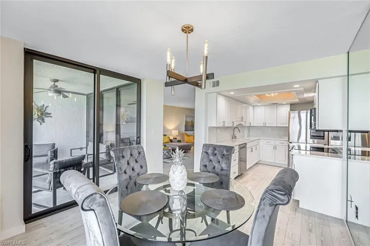 Dining room with light wood-style flooring, a raised ceiling, a wall of windows, a chandelier, and recessed lighting