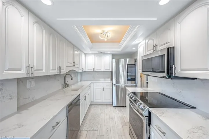 Kitchen with decorative backsplash, stainless steel appliances, light stone counters, light wood-style flooring, and white cabinets