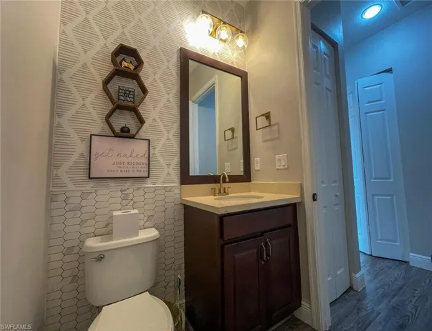 Bathroom with tile walls, hardwood / wood-style floors, vanity, and toilet