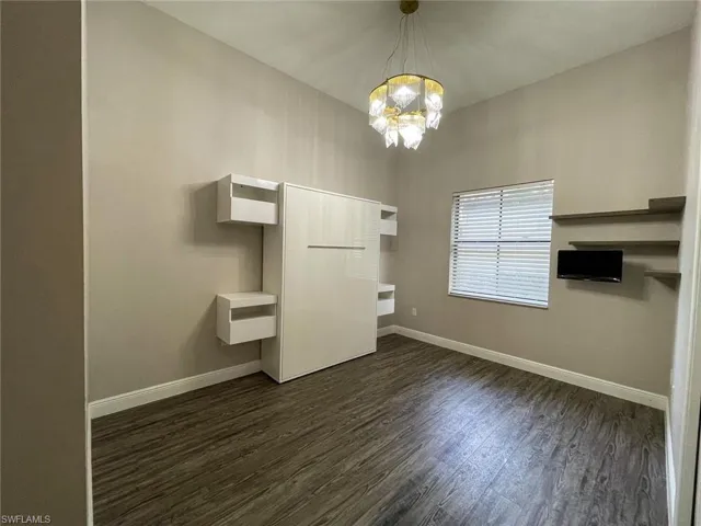 Unfurnished bedroom featuring an inviting chandelier and dark wood-type flooring