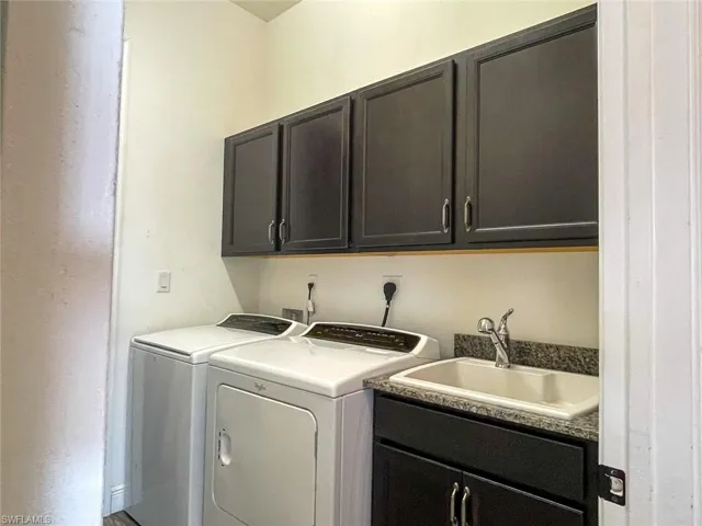 Laundry area with washer and clothes dryer, cabinets, and sink