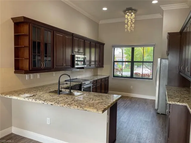 Kitchen with kitchen peninsula, light stone counters, appliances with stainless steel finishes, and sink