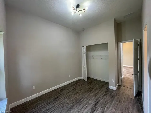 Unfurnished bedroom featuring a textured ceiling, a closet, and dark wood-type flooring