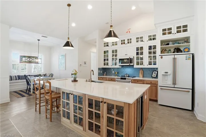 Two tone kitchen featuring glass fronted cabinets, two tone cabinetry, hanging light fixtures, high end appliances, and a breakfast bar area