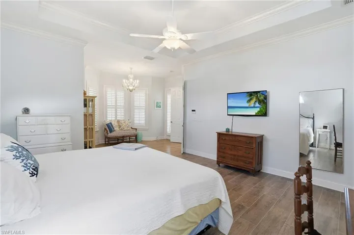 Bedroom featuring a raised ceiling, wood tiled floors, ceiling fan, a chandelier, and crown molding