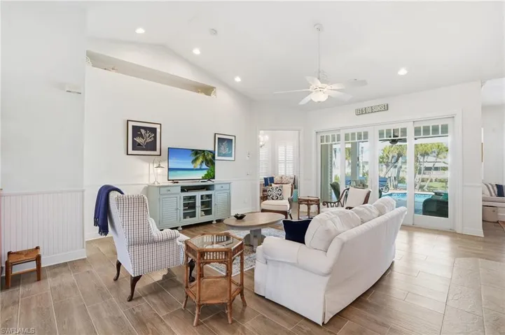 Living room with wood finish floors, a ceiling fan, recessed lighting, lofted ceiling, and wainscoting