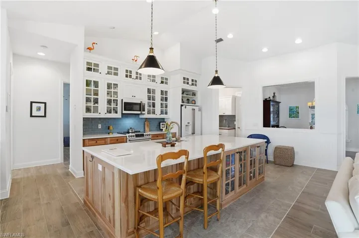 Dual tone kitchen featuring glass insert cabinets, two tone cabinets, hanging light fixtures, wood tiled floors, and a large island