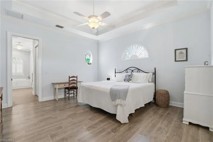 Bedroom featuring wood tiled floors, a raised ceiling, ceiling fan, and crown molding