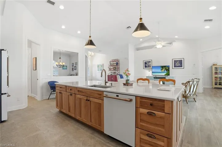 Kitchen with wood finish cabinetry, white appliances, pendant lighting, a kitchen island with sink, and vaulted ceiling