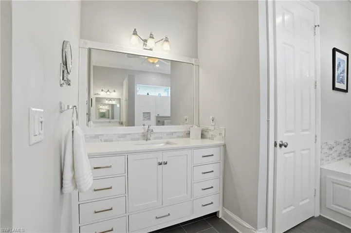 Bathroom with tasteful backsplash, vanity, dark tile patterned flooring, and a bath