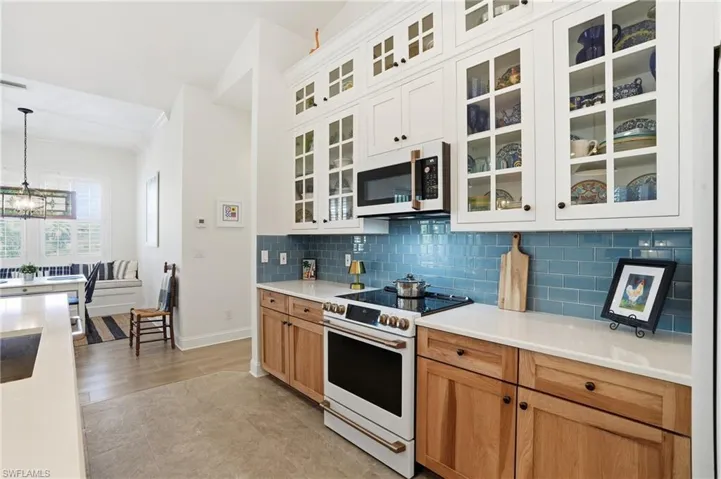 Kitchen featuring dual tone cabinetry, white appliances, glass insert cabinets, backsplash, and suspended lighting