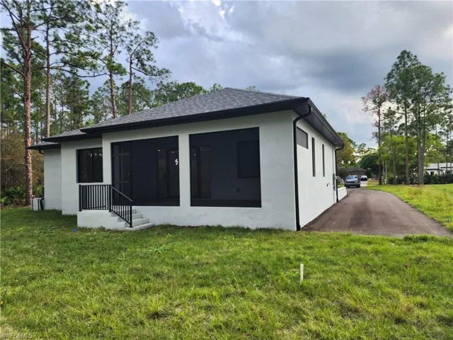 Back of house with a yard, stucco siding, roof with shingles, and a sunroom