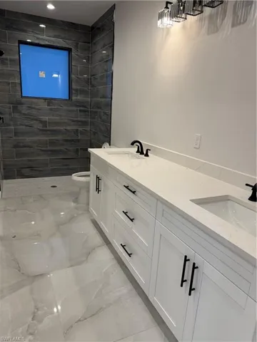 Bathroom featuring double vanity, light marble finish floors, and a tile shower