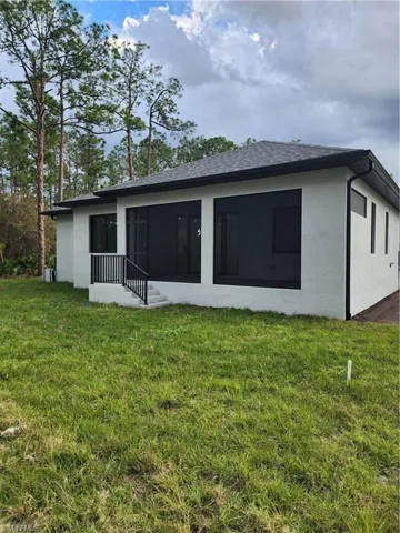Rear view of house with a yard, stucco siding, and a sunroom