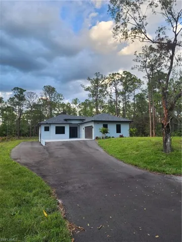 View of front of property with asphalt driveway, a front lawn, roof with shingles, and view of wooded area